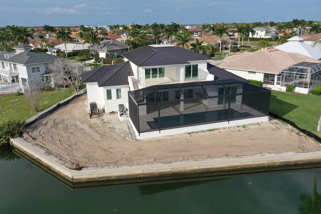 Aerial view of a waterfront home under construction with a screened pool enclosure