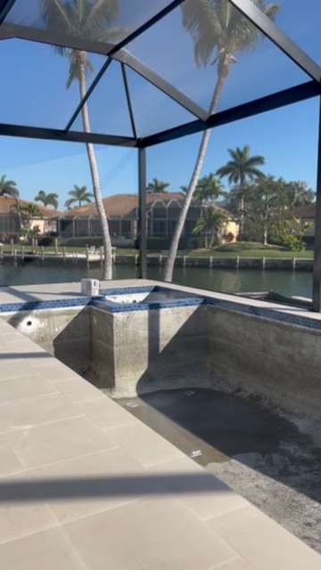 Pool shell under construction inside a screened enclosure on the canal